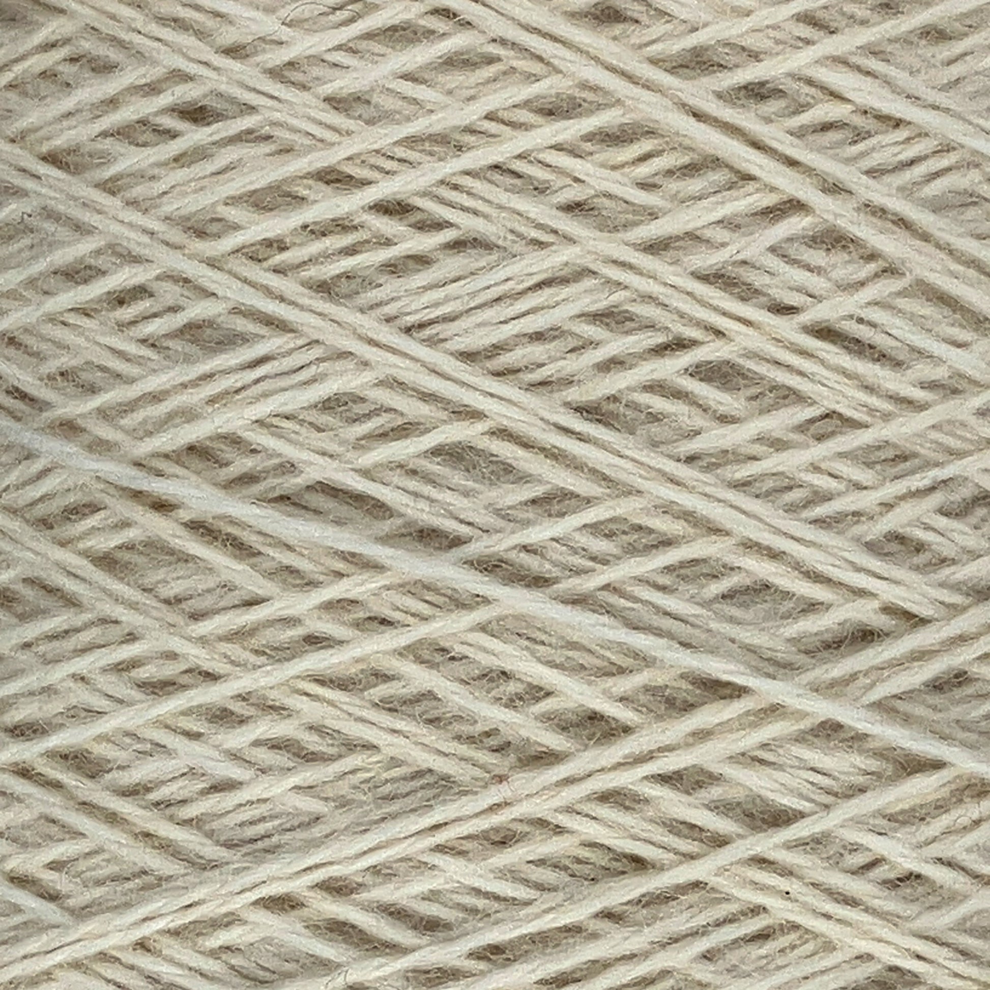 Close-up image of JaggerSpun Heather 3/8 wool yarns from Jagger Brothers, Inc. neatly wound into a ball. The beige-colored strands are tightly arranged in a crisscross pattern, highlighting the texture and fine fibers of the worsted spun yarn.