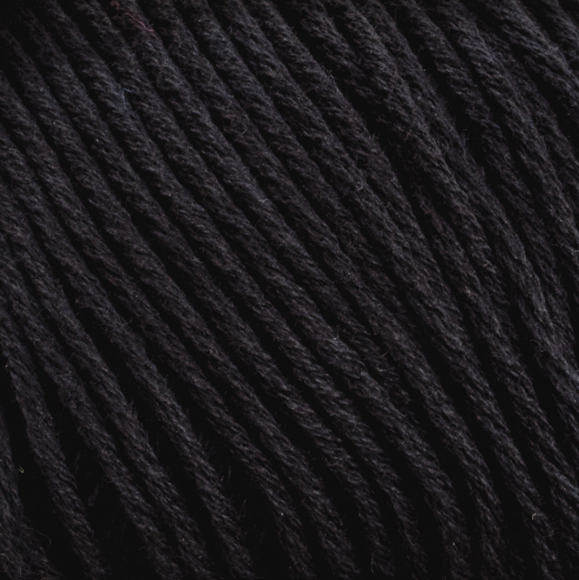 Close-up image of tightly wound, dark-colored Cotton Fleece by Brown Sheep, showing the detailed texture and strands of the material. The color appears to be a deep black, highlighting the twists and fibers in the yarn, making it perfect for intricate knitting patterns.