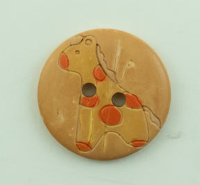 The Baby Button by Buttons Etc. is a 13/16" diameter, round, light brown button featuring an engraved and painted design of a giraffe. The giraffe is outlined with red and orange spots and has two holes in the middle. The button's surface shows signs of slight wear.