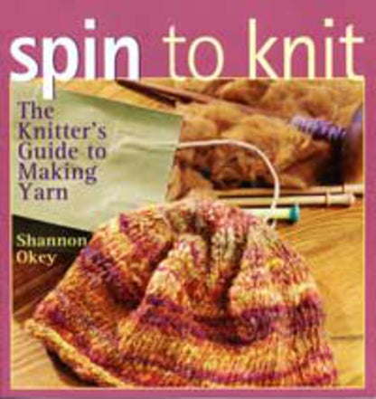 The image displays the cover of "Spin to Knit The Knitter's Guide to Making Yarn" by Shannon Okey, a book published by Golden Peak Media. The cover art features a partially knitted multicolored item with knitting needles and spinning equipment set against a pink backdrop.