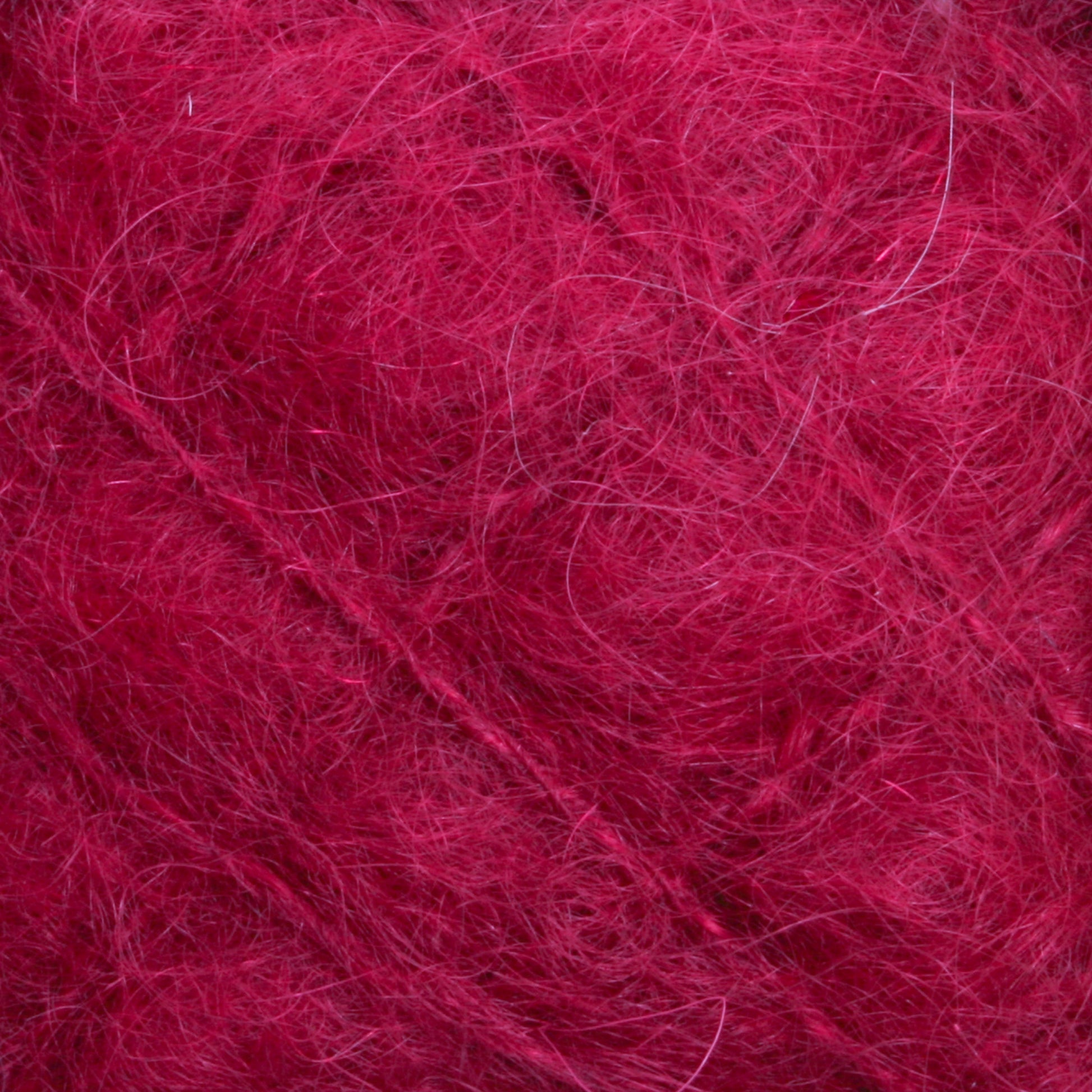 Close-up of the Victorian Brushed Mohair Yarn | Mini Skein from Caledonian Dye Works in pink/red showcases numerous fine fibers creating a textured, soft appearance. The vibrant color adds richness to the tangled threads, highlighting the intricate, hairy details of luxurious mohair.