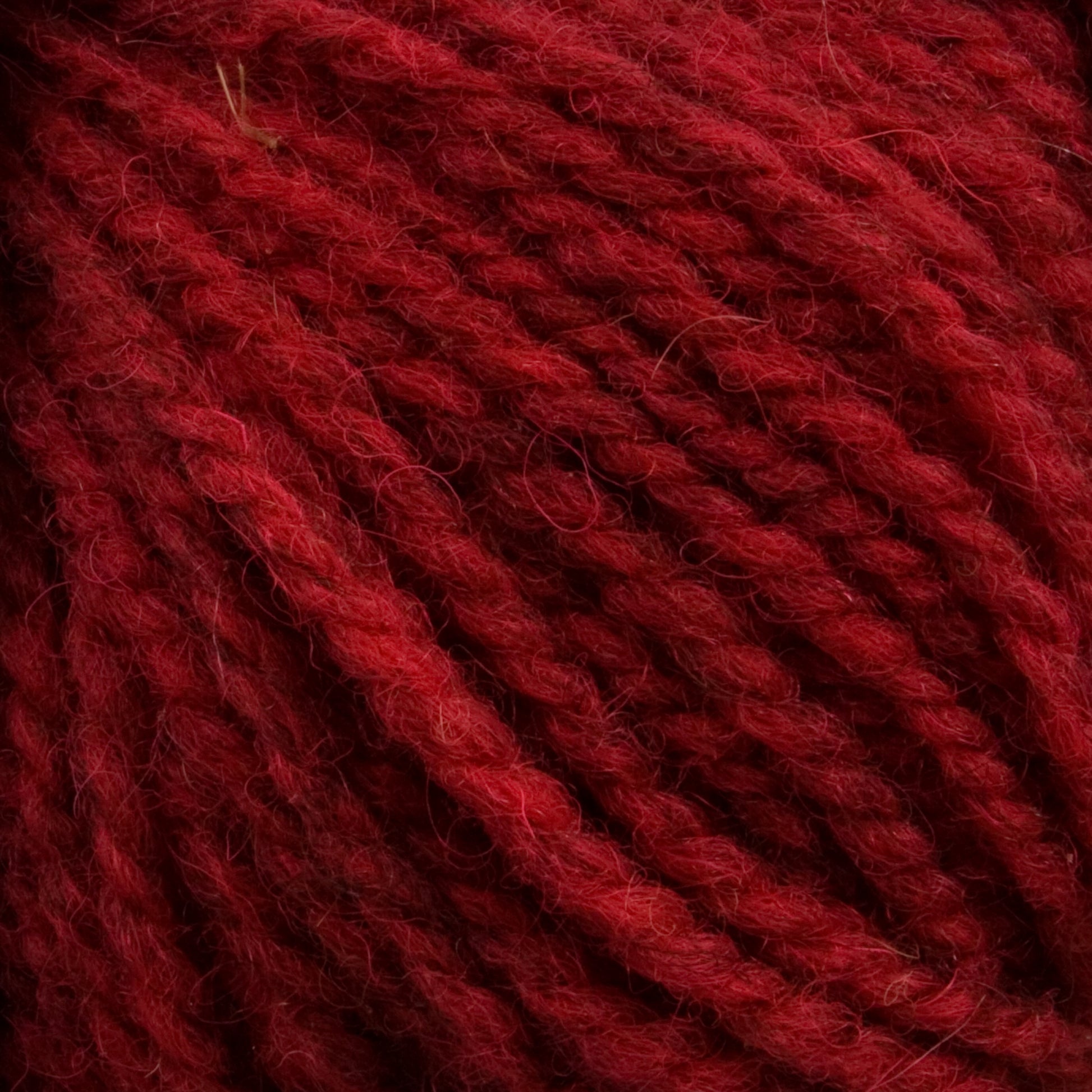 Close-up image of thick, twisted red Tuffy Canadian Sock Yarn by Briggs & Little showing its fibrous texture and deep, rich color. The intertwined strands create a detailed and tactile visual, highlighting the worsted weight yarn's robustness and suitability for knitting or crocheting cozy winter socks.