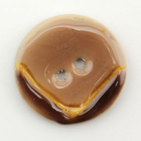 A close-up image of the Coco Boomerang 1 1/8" Button by Buttons Etc. showcases a charming brown button with two holes and a smooth, glossy shellac finish. The design resembles a smiling face, where the holes appear as eyes and a painted curved line serves as the mouth. This delightful button, reminiscent of traditional coconut buttons, stands out against the plain white background.