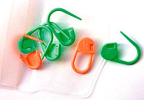 Several green and orange Locking Ring Stitch Markers from Accessories Unlimited, commonly used in knitting and crochet, are scattered on a white surface. The stitch markers, shaped like small safety pins, are perfect for bulky yarns and large needles. They are next to a transparent plastic case.