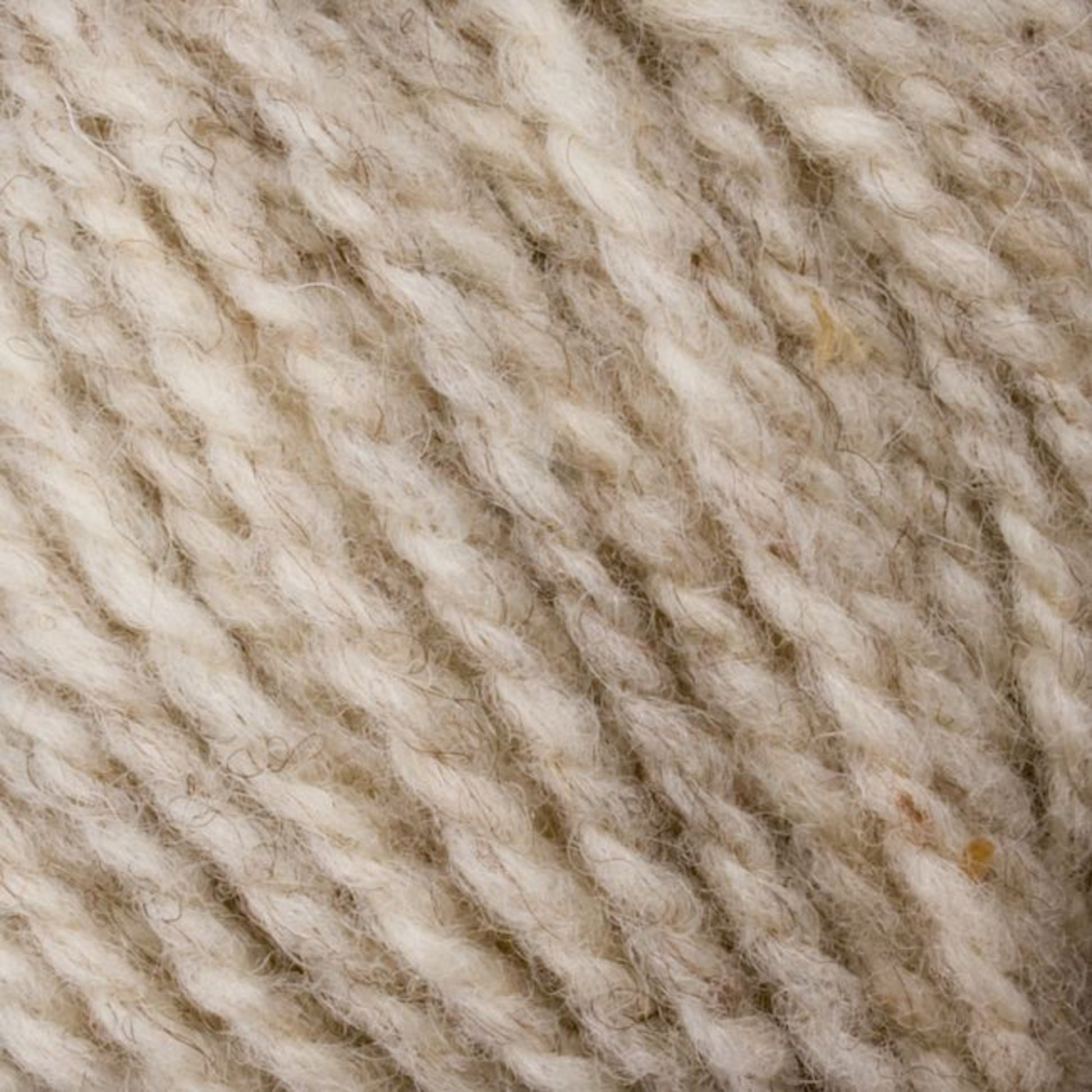 Close-up of beige and cream twisted yarn fibers. The texture is soft and fluffy, with a mixture of thick and thin strands. Made from Bartlettyarns Maine Wool - Sport, this yarn has natural fibers that give it a slightly uneven, rustic appearance enhanced by subtle heathered colors.