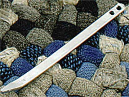 A silver steel tent stake with two holes near the top lies on a textured, woven surface composed of various shades of blue, gray, and brown fabric, reminiscent of patterns created with Whitman Tool & Die Co., Inc.'s Braidkin Lacer.