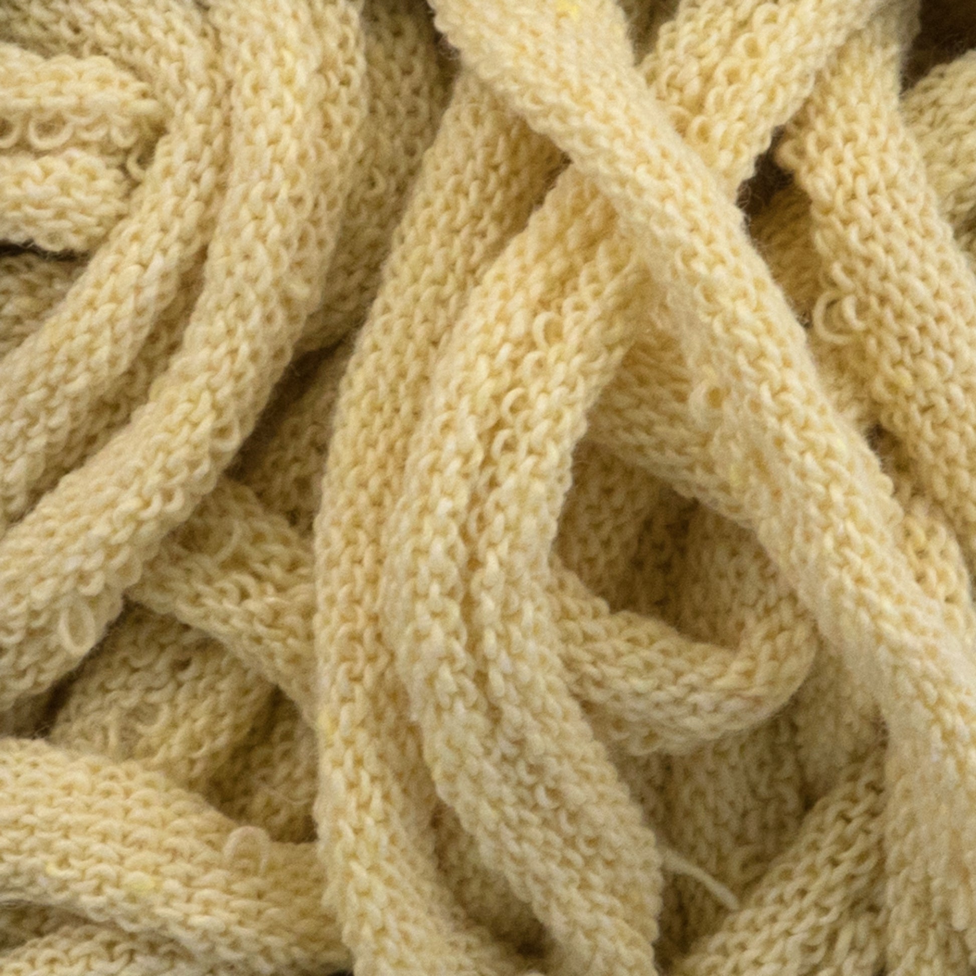 A close-up view of a tangled mass of thick, cream-colored yarn. The texture is highly detailed, showcasing the knitted pattern and soft, woolen material reminiscent of Harrisville Potholder Loops from Friendly Loom’s Traditional Size Mini Pack, meticulously woven on a potholder loom.