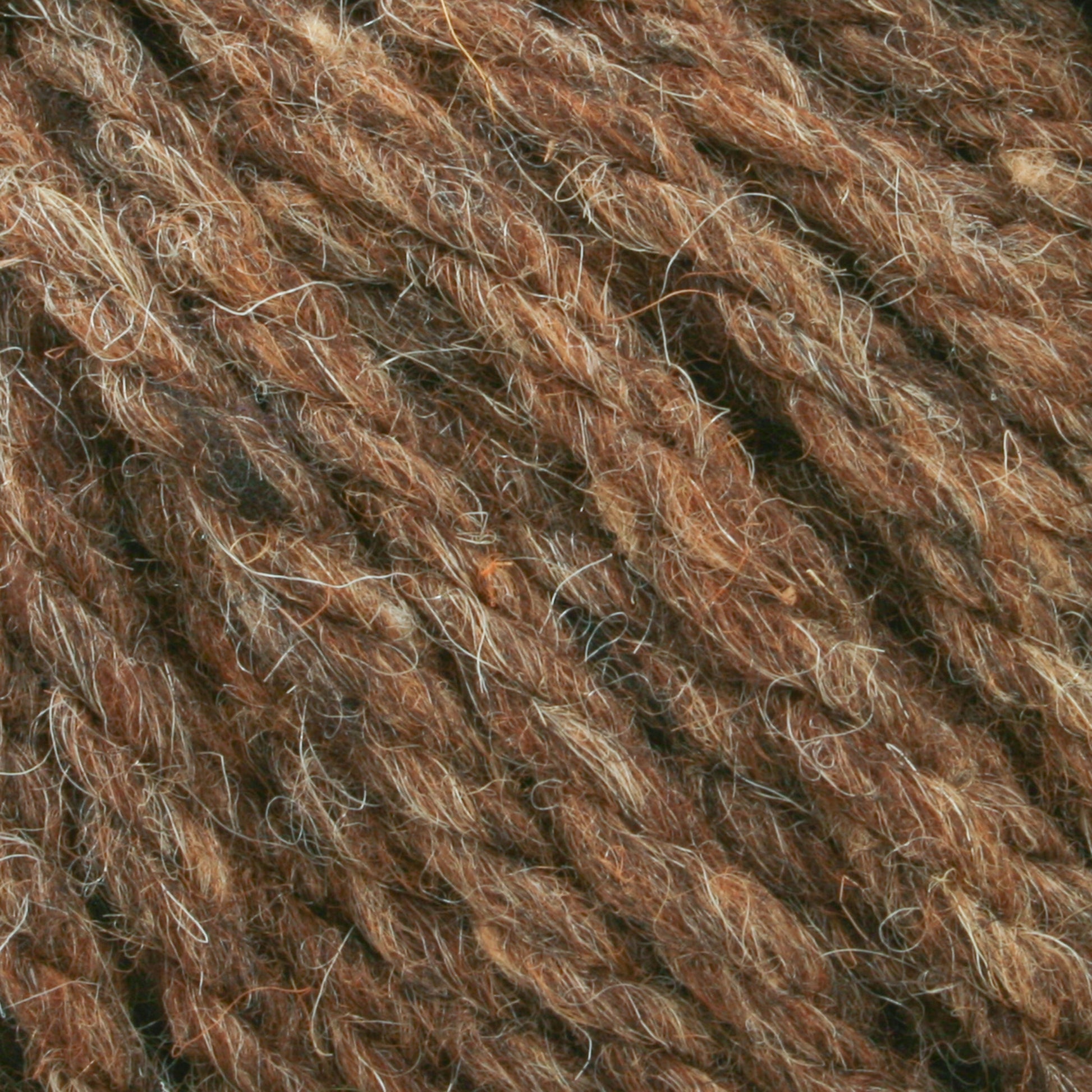 Close-up of twisted Halcyon Yarn Classic Rug Wool from Caledonian Dye Works, showcasing a blend of dark and light brown hues. The texture appears soft and fluffy, with individual strands of fiber visible. This hand-dyed yarn offers a natural, rustic look suitable for knitting, crocheting projects, or even Classic Rug Wool creations.