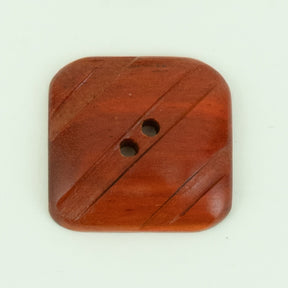 The Wood Grooved Square Button by Buttons Etc. is a wooden button with rounded edges and two central holes. Measuring 1 3/8" across, it sports diagonal grooves on its surface for a textured look. The polished wood has a medium-brown finish.