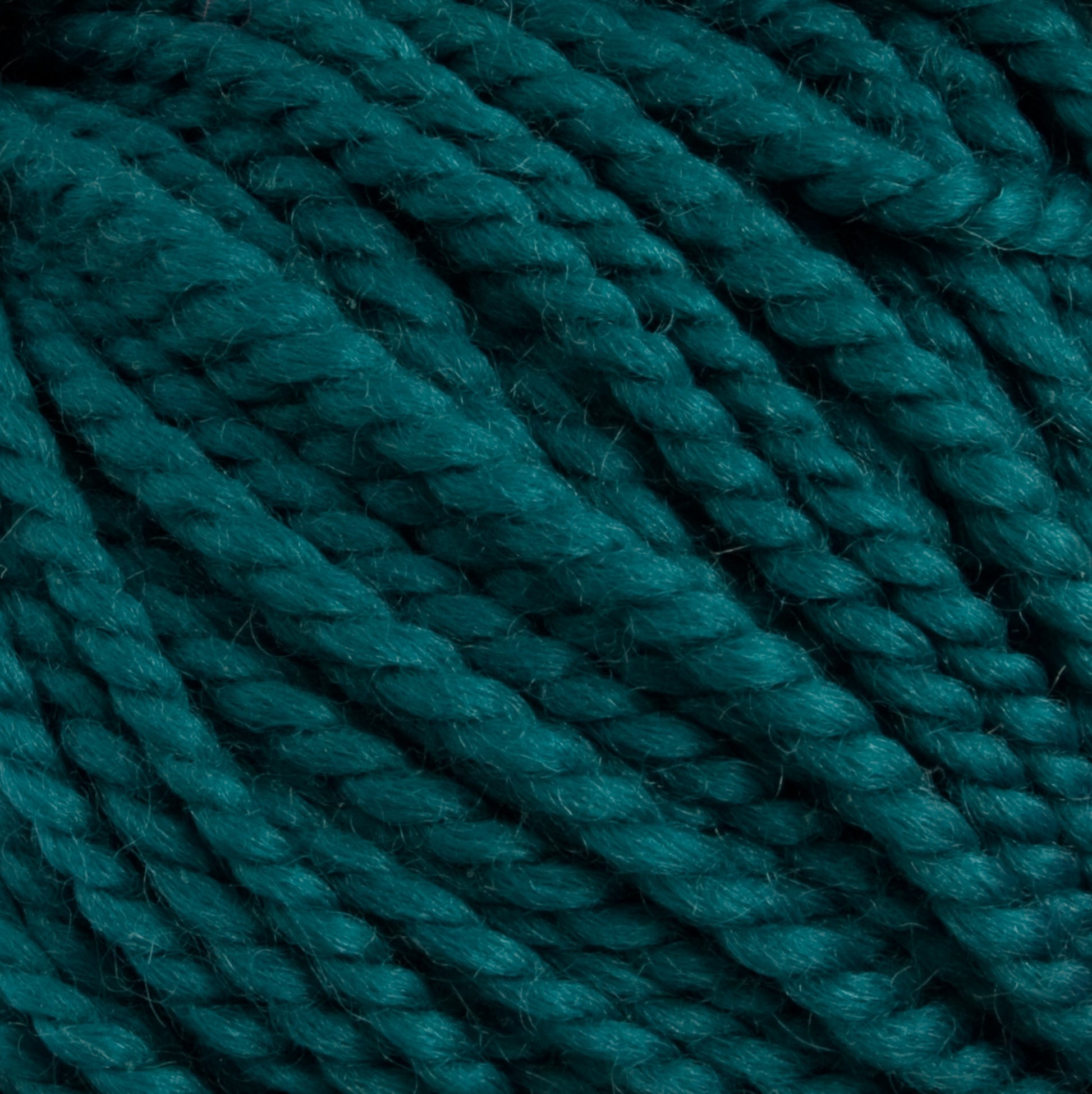 Close-up image of tightly wound, teal-colored Norumbega Aran weight yarn strands from Caledonian Dye Works. The texture showcases the 100% U.S. wool's soft and slightly fuzzy surface, twisted into thick, consistent ropes. The overall appearance is vibrant and richly hued.