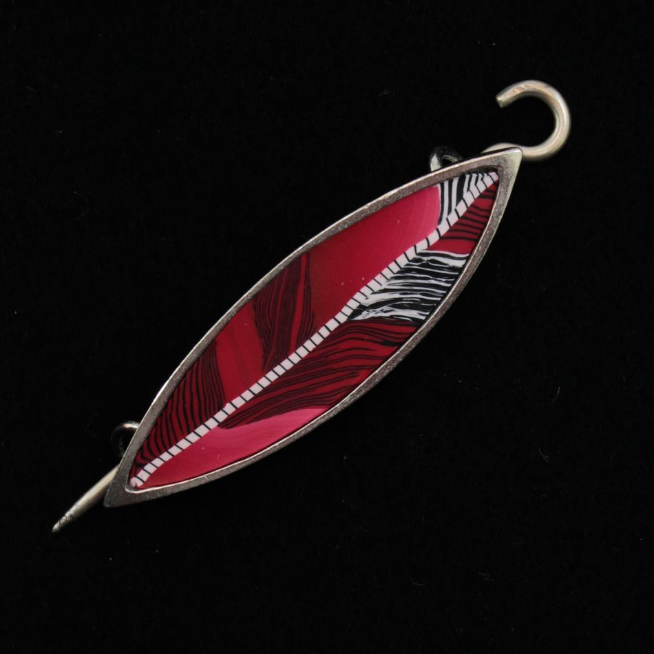 The Songbird Shawl Pin by Bonnie Bishoff Designs, crafted by Bonnie Bishoff, is a handmade metal brooch shaped like a leaf with a striking red and white striped pattern set against a black background. It features a secure locking pin for easy attachment, making it the perfect gift.