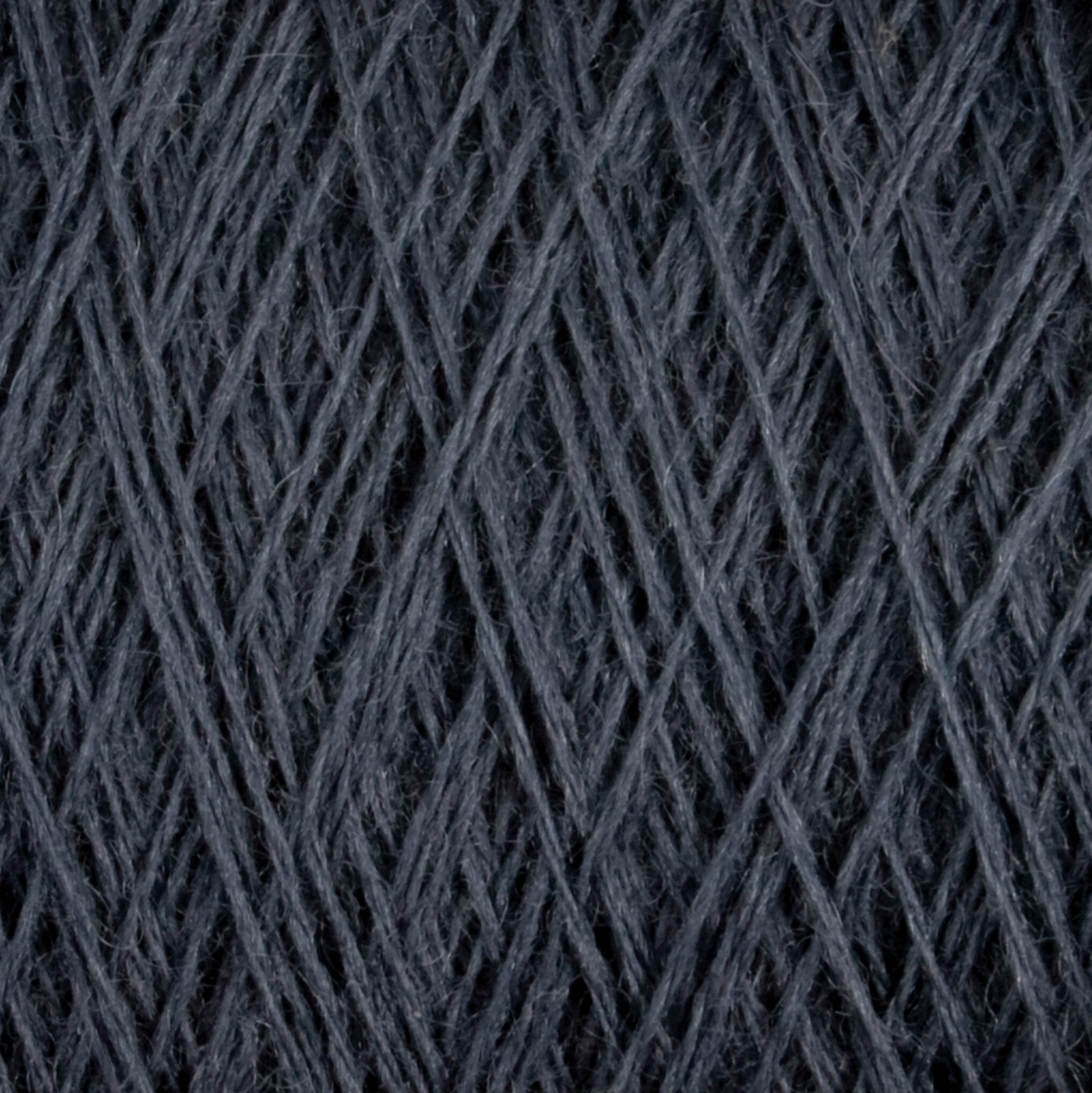 Close-up image of dark grey Jagger Brothers, Inc. JaggerSpun Maine Line 3/8 Yarn wound into a dense ball. The strands are tightly interwoven, creating a textured pattern of crisscrossing lines. The soft medium grade wool appears slightly fuzzy, enhancing its cozy appeal.