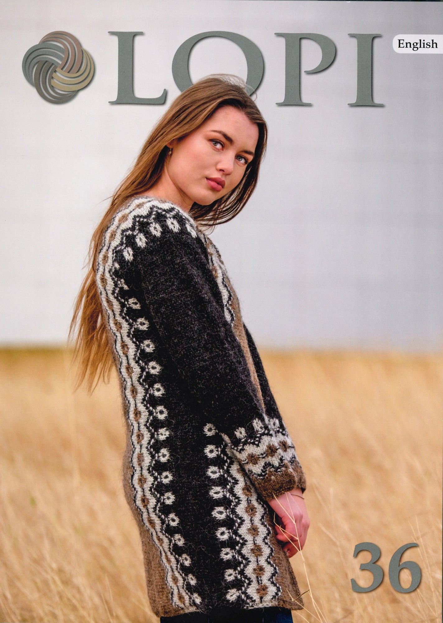 A woman with long hair is wearing a woolen cardigan adorned with intricate patterns while standing in a field of tall grass. The cover prominently displays the text "LOPI" at the top along with a yarn logo, and "36" at the bottom right corner. The word "English" is also visible in the top right corner. This product is titled Lopi Volume 36 by Berroco, Inc.