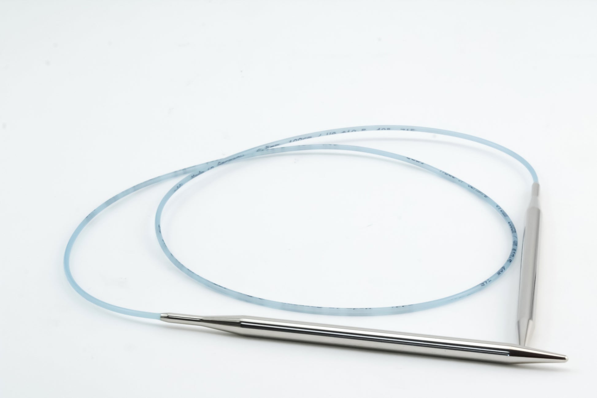 A coiled, light blue Addi Turbo Circular Knitting Needle by Skacel, featuring a metallic, pointed tip on each end, reminiscent of traditional Addi Turbo needles, placed on a plain white surface. The needle has faint markings along its length.