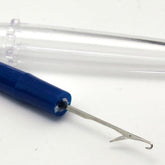 The Knit Picker by Dritz from Notions, featuring a blue handle, commonly used as a snag repair tool, is shown alongside its transparent plastic cover, both placed on a pristine white surface.