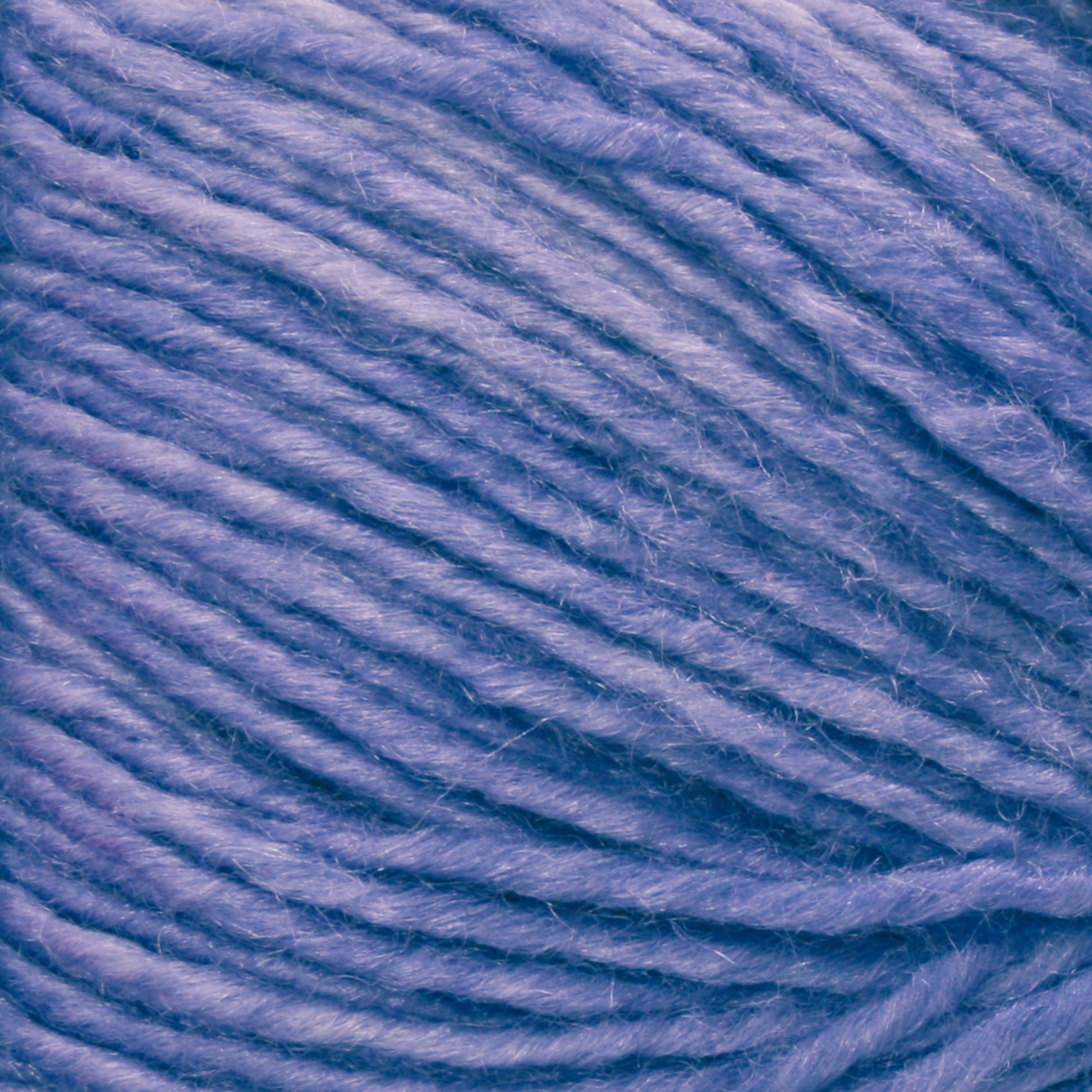 A close-up view of a spool of Malabrigo Silky Merino yarn, showing the texture of the intertwined fibers in detail. The luxury yarn from Malabrigo Yarn appears soft and thick, with a subtle sheen reflecting light on the surface.