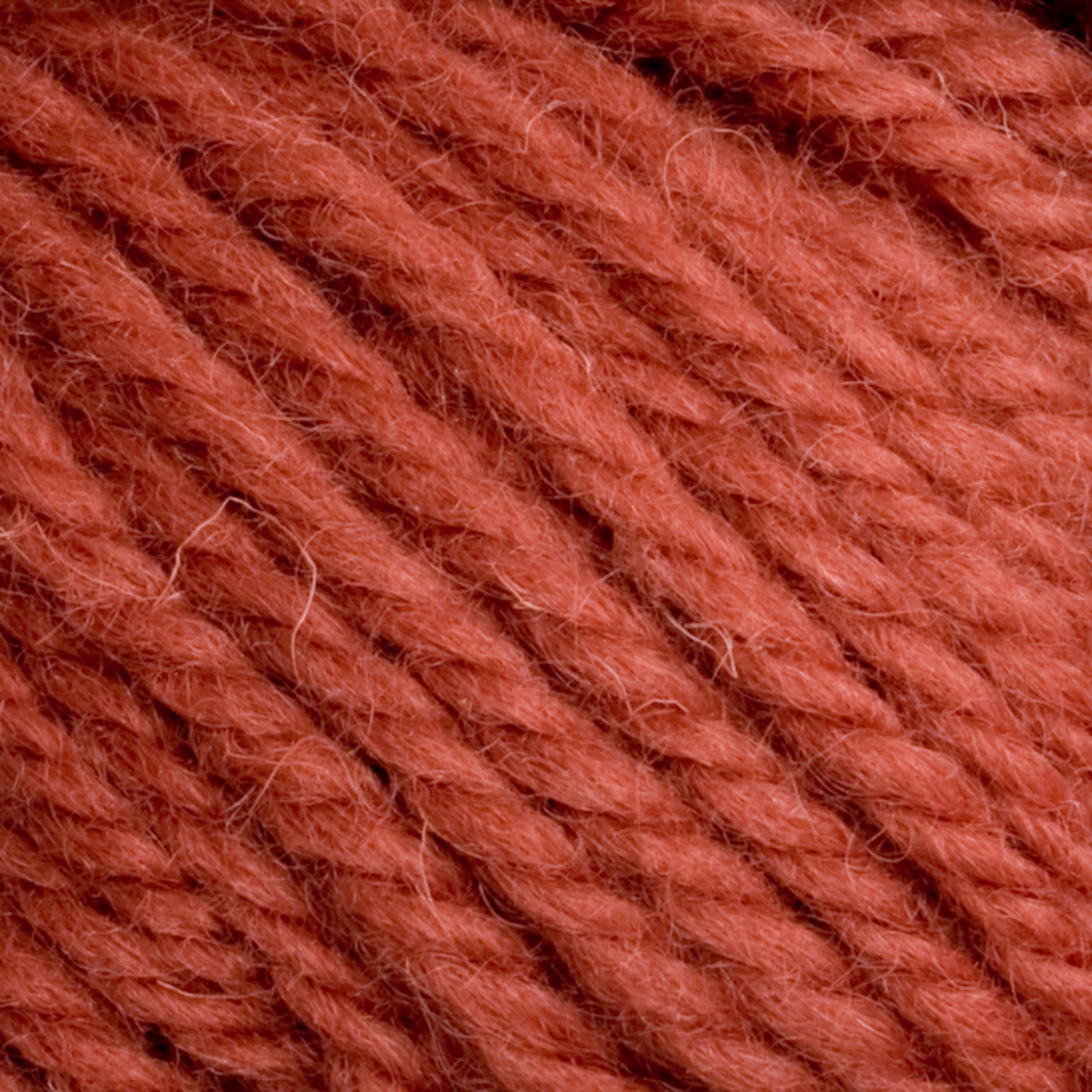 Close-up image of soft, thick red-orange Halcyon Yarn Classic Rug Wool fibers from Caledonian Dye Works intertwined, showing the detailed texture and strands. The yarn appears fluffy and tightly wound, creating a rich and vibrant appearance suitable for knitting or crocheting projects—reminiscent of the traditional rug wool used by weavers.