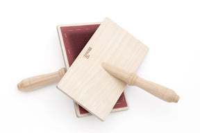 A pair of wooden wool carders with red carding cloths, used for preparing wool for spinning, lie crossed on a white background. One carder is face-up, showing the brand name "Kromski North America," while the other is face-down, revealing the handle.