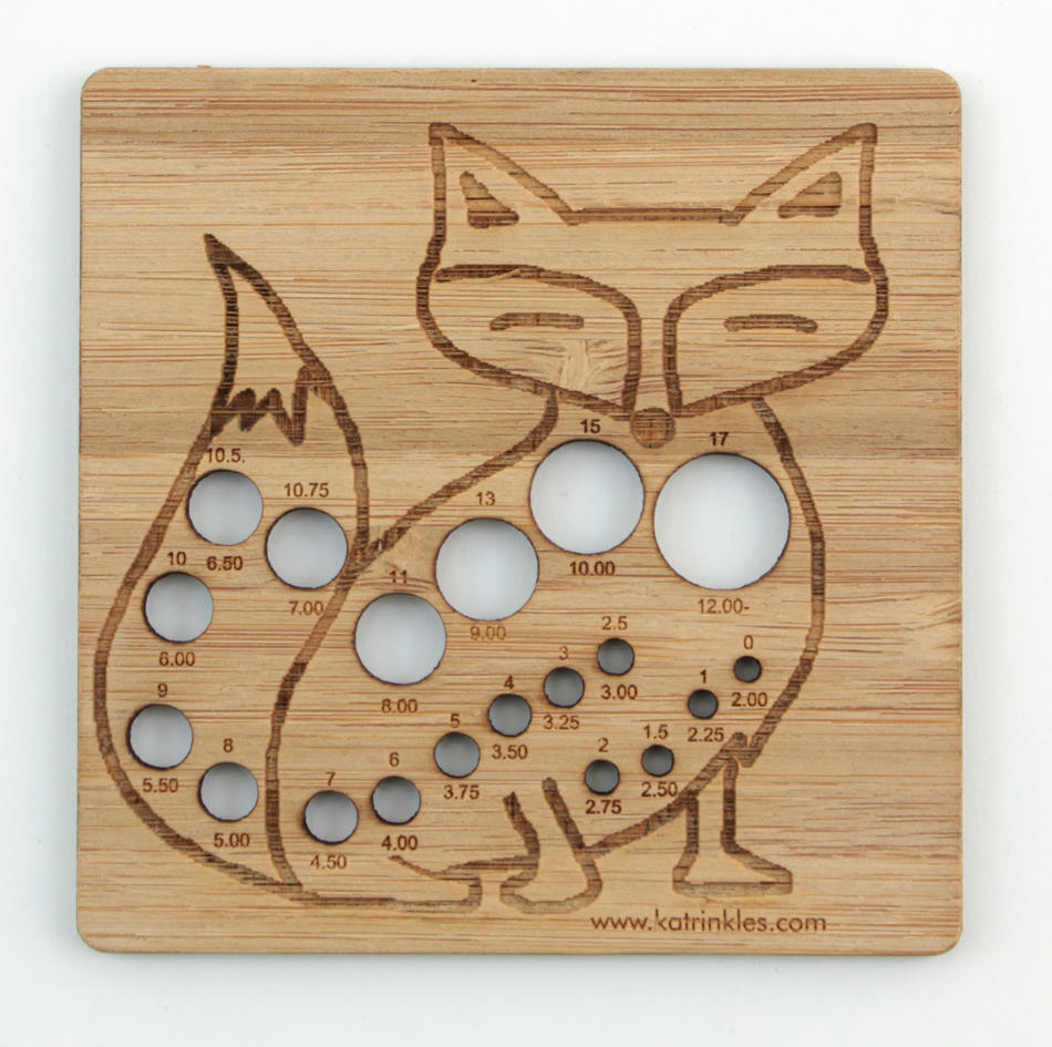 The Never Not Knitting Animal Needle Gauge is a wooden knitting needle gauge shaped like a fox, crafted from laser-cut bamboo. This gauge features multiple circular holes labeled with sizes ranging from 2.00 mm to 15.00 mm, and etched details on the face, body, and tail accentuate its design. The bottom is inscribed with "katrinkles.com"—an ideal tool for Animal Needle Gauges enthusiasts.