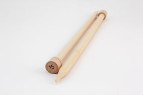 A pair of Bamboo Single-Point Knitting Needles from Accessories Unlimited lies crossed on a white background. The larger ends are marked with the number 15, indicating their size. The 12" needles are light-colored and smooth, with one end pointed and the other featuring a flat knob.