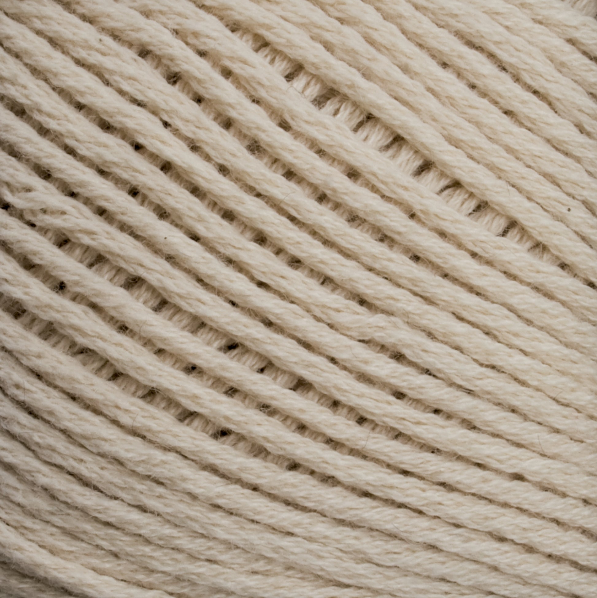 Close-up image of a coiled ball of off-white Cotton Fleece yarn from Brown Sheep, showing the texture and tightly wound fibers in detail. The strands run diagonally across the image, highlighting the soft and natural appearance of the yarn, perfect for creating delicate knitting patterns.