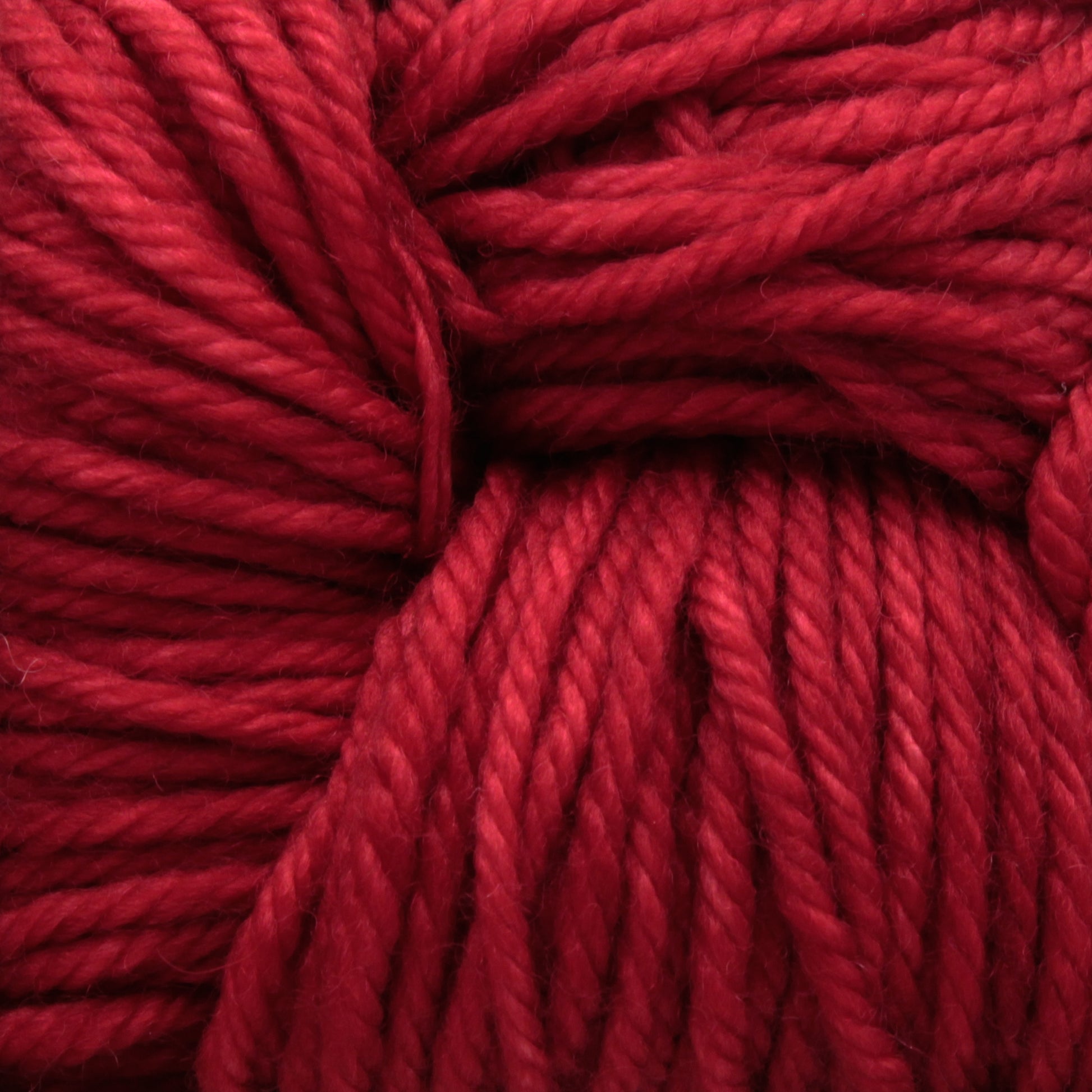 Close-up image of thick, vibrant red Malabrigo Rios yarn tangled together. The strands have a glossy texture and a slightly twisted appearance, indicating a soft and plush feel. The image showcases the rich kettle-dyed colors and detailed texture of the yarn by Malabrigo Yarn.