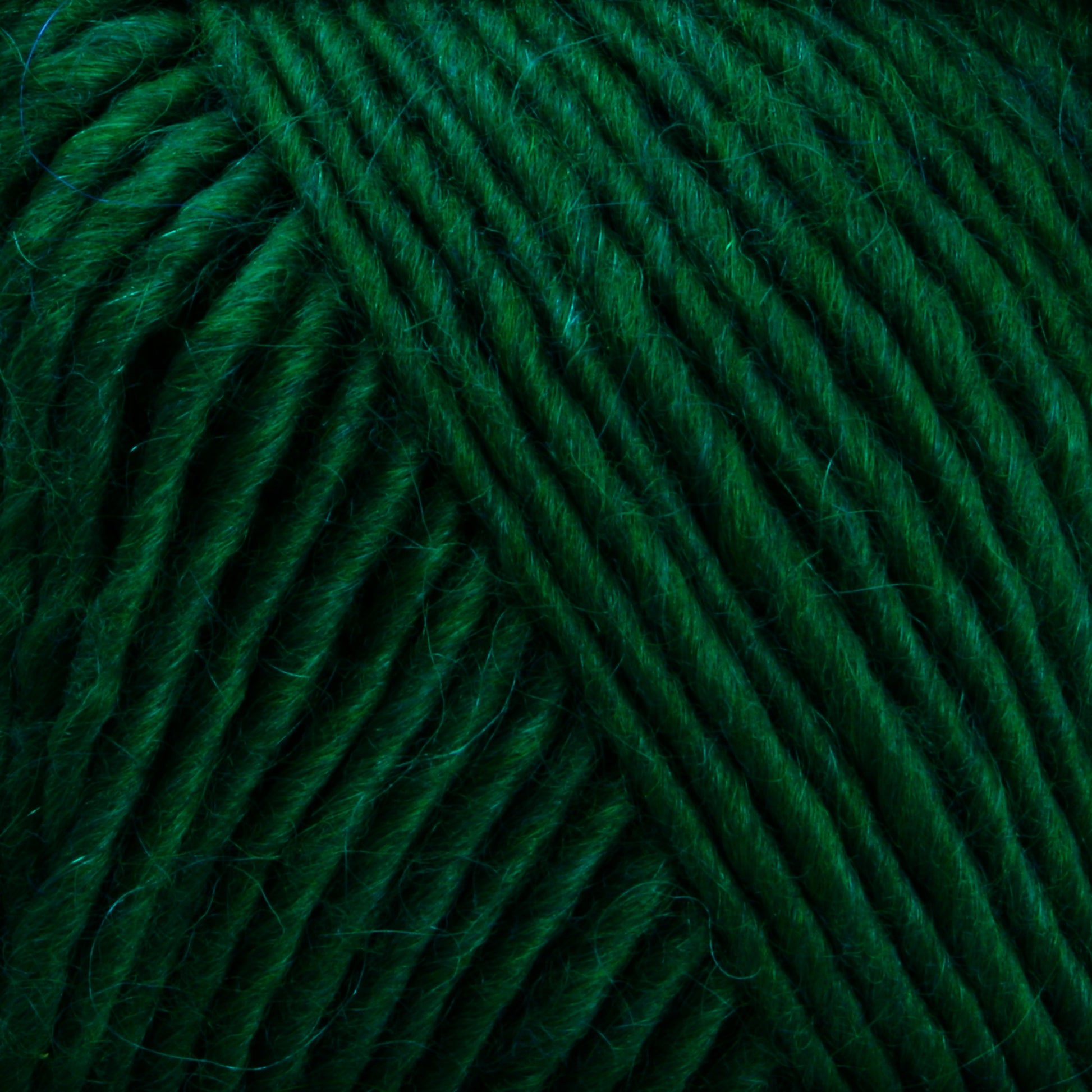 Close-up view of a ball of Lamb's Pride Worsted Yarn by Brown Sheep, showcasing the soft, textured fibers and tightly wound strands. The rich green color and fluffy texture suggest it is suitable for warm, cozy knitting or even felting projects.