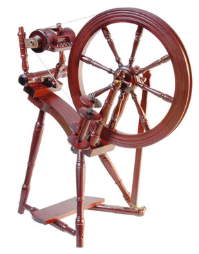 The Kromski Prelude Spinning Wheel by Kromski North America is a traditional wooden Single Drive wheel featuring a large circular wheel connected to smaller components, including a treadle and spindle. Crafted from European alder and birch, the polished wood boasts intricate turned details, giving it a classic, handcrafted appearance characteristic of Kromski wheels.