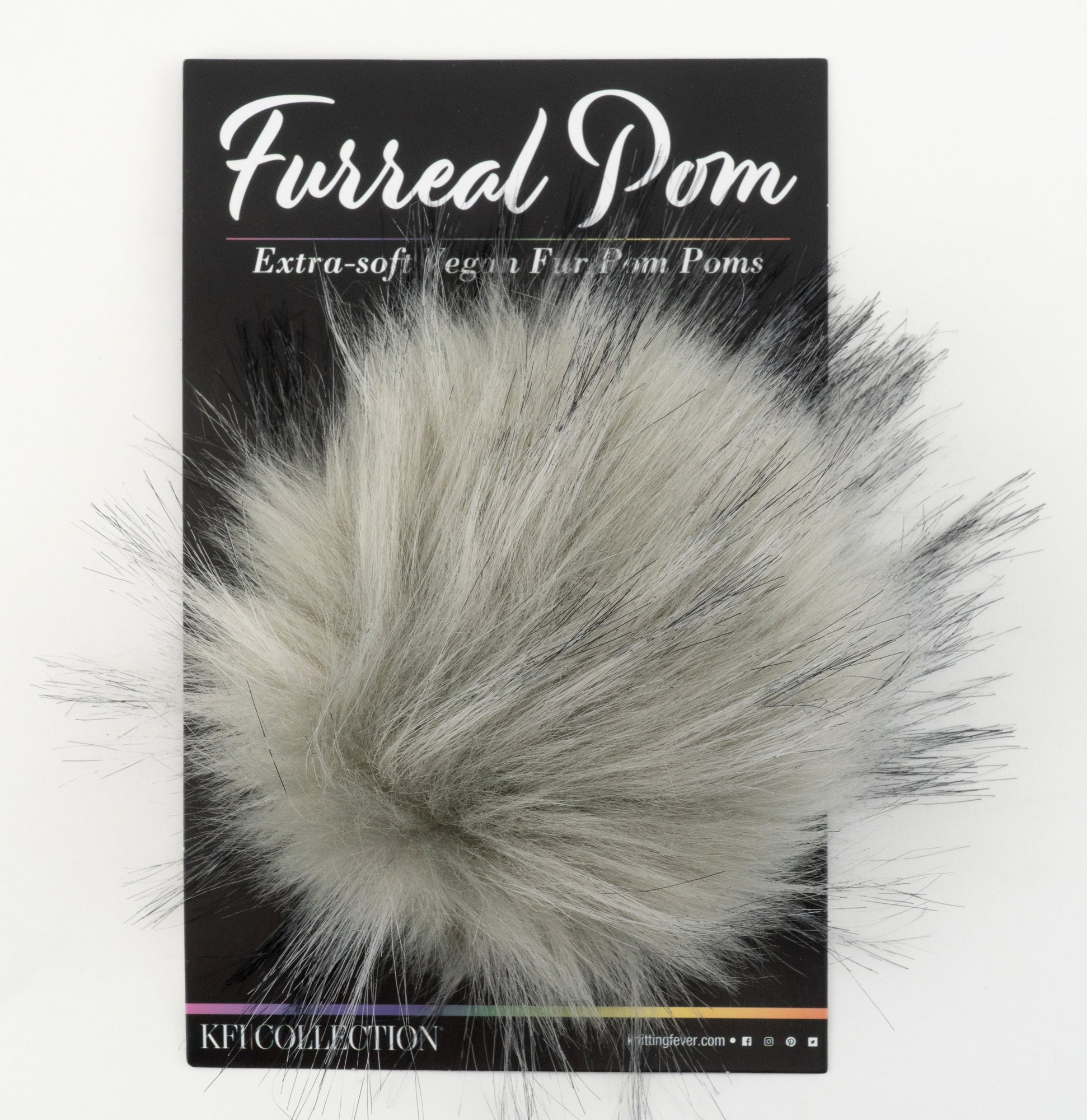 A package labeled "Furreal Pom by KFI" from Knitting Fever / Euro Yarns displays a fluffy, gray faux fur pompom attached to a black backing card. The text on the packaging reads "Extra-soft Vegan Fur Pom Poms" and "KFI Collection." The pompom has a soft, wispy texture with varying shades of gray.