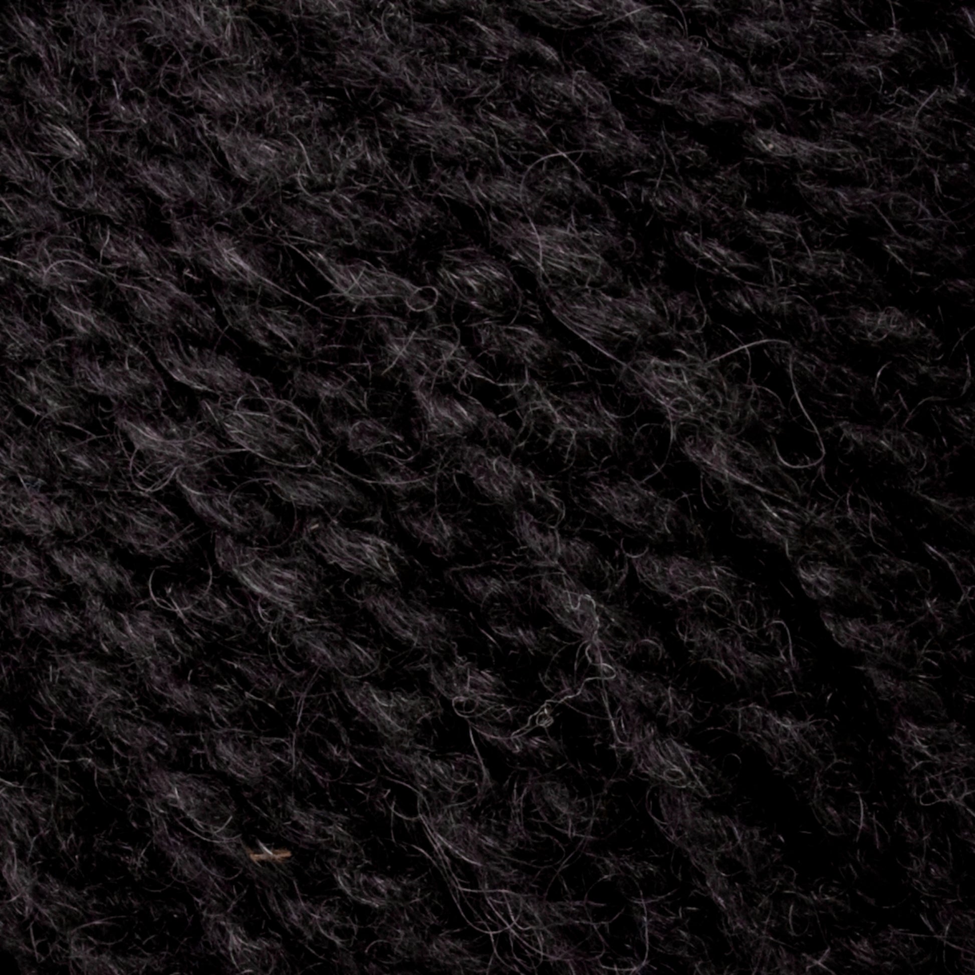 Close-up image of dark black yarn, showcasing its textured fibers and twisted strands. The Bartlettyarns Maine Wool Yarn appears soft and slightly fuzzy, with a dense and uniform pattern, characteristic of worsted weight yarn. Subtle heathered colors add depth to the elegant black hue.