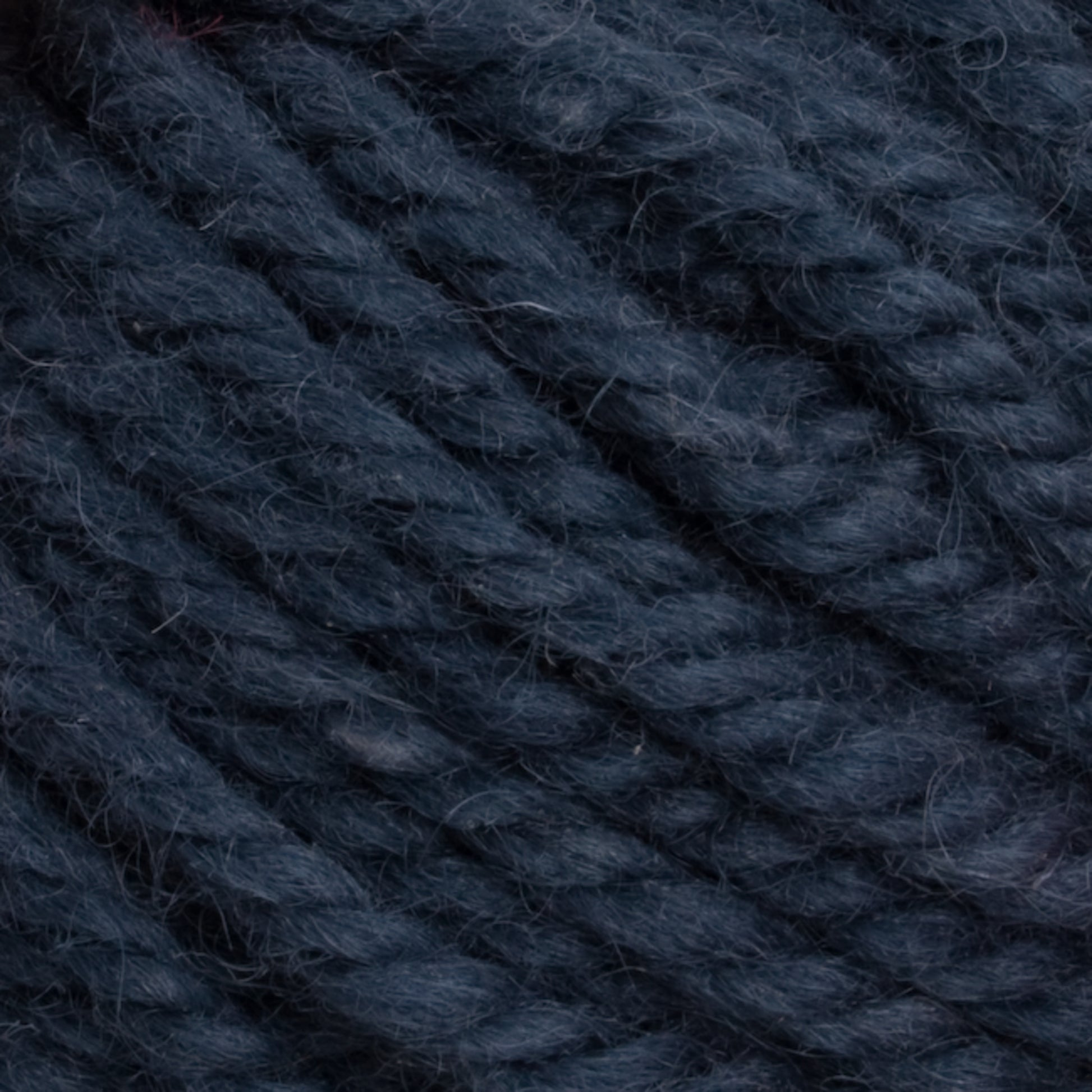 Close-up image of thick, dark blue Halcyon Yarn Classic Rug Wool by Caledonian Dye Works. The yarn appears textured with tightly twisted strands and subtle variations in shade, giving it a soft and fluffy appearance. This image highlights the rich color and fibrous detail of the hand-dyed wool, perfect for dedicated weavers.