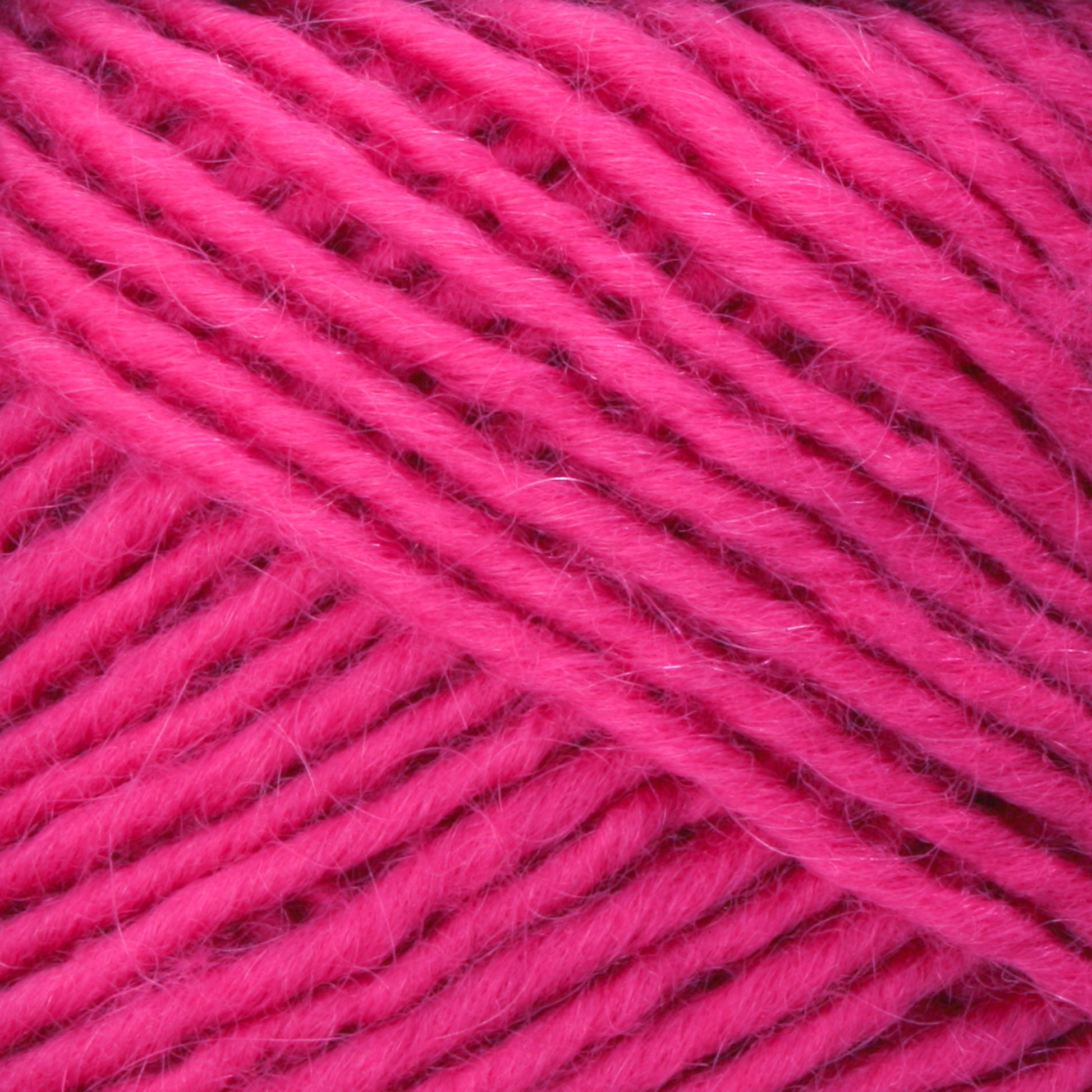 Close-up of Lamb's Pride Bulky Yarn in bright pink. The image showcases the soft, fibrous texture and the tight, even strands of this Brown Sheep yarn, indicating that it is well-spun and perfect for knitters and crocheters to create beautiful projects such as woven blankets or Icelandic sweaters.