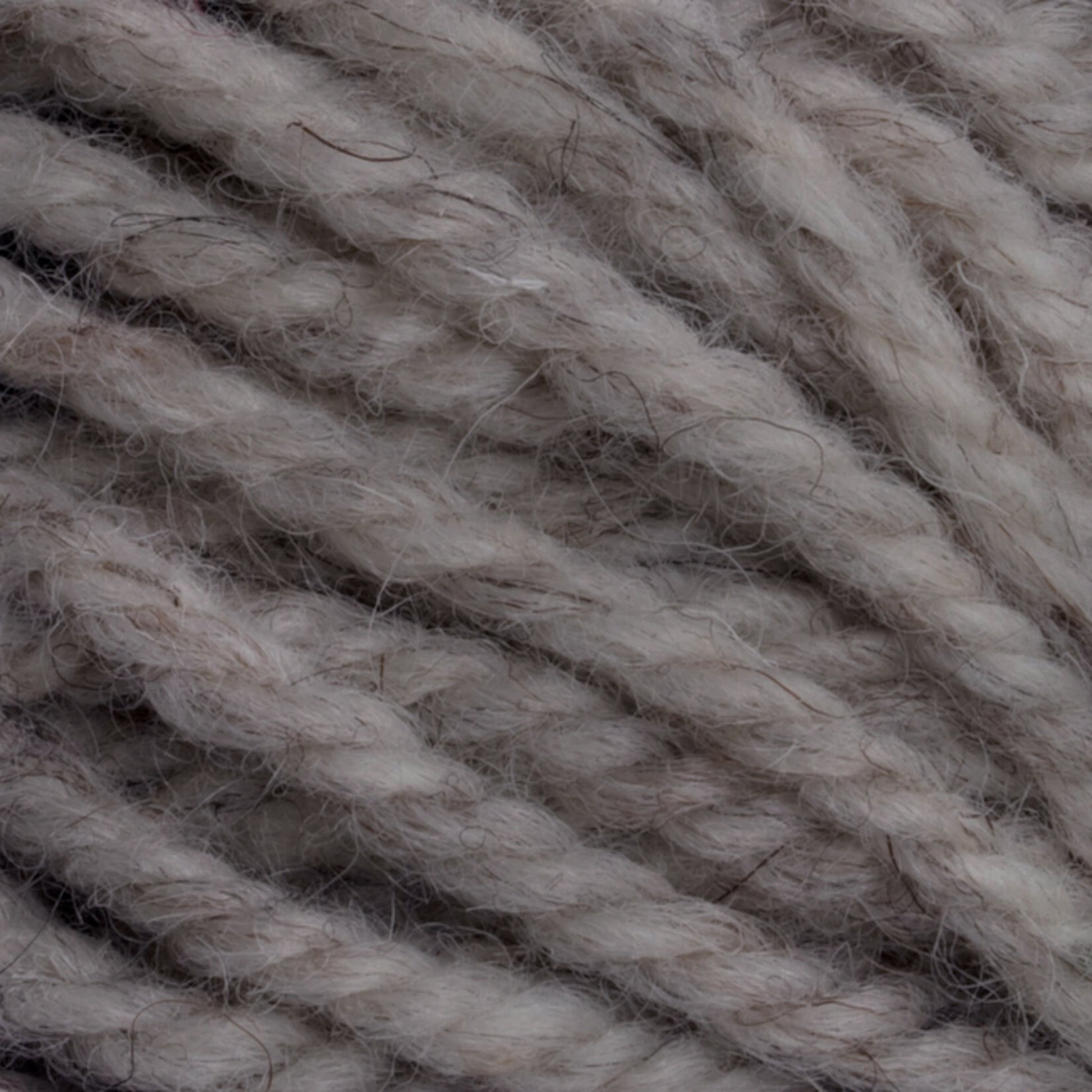 Close-up image of thick, twisted Halcyon Yarn Classic Rug Wool | Strand in a taupe color. The yarn, produced by Caledonian Dye Works, has a slightly fuzzy texture with visible fibers extending from the strands, giving it a cozy and natural appearance. Ideal for rug weavers, this Classic Rug Wool fills the background, highlighting its detailed texture.