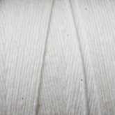 Close-up image of Maurice Brassard's Cotton 8/8 Carpet Warp wrapped around a reel. The texture of the yarn is clearly visible, showcasing its fibrous and soft appearance with slight variations in thickness. The light highlights the delicate threads intertwining, perfect for knitting and crochet projects.