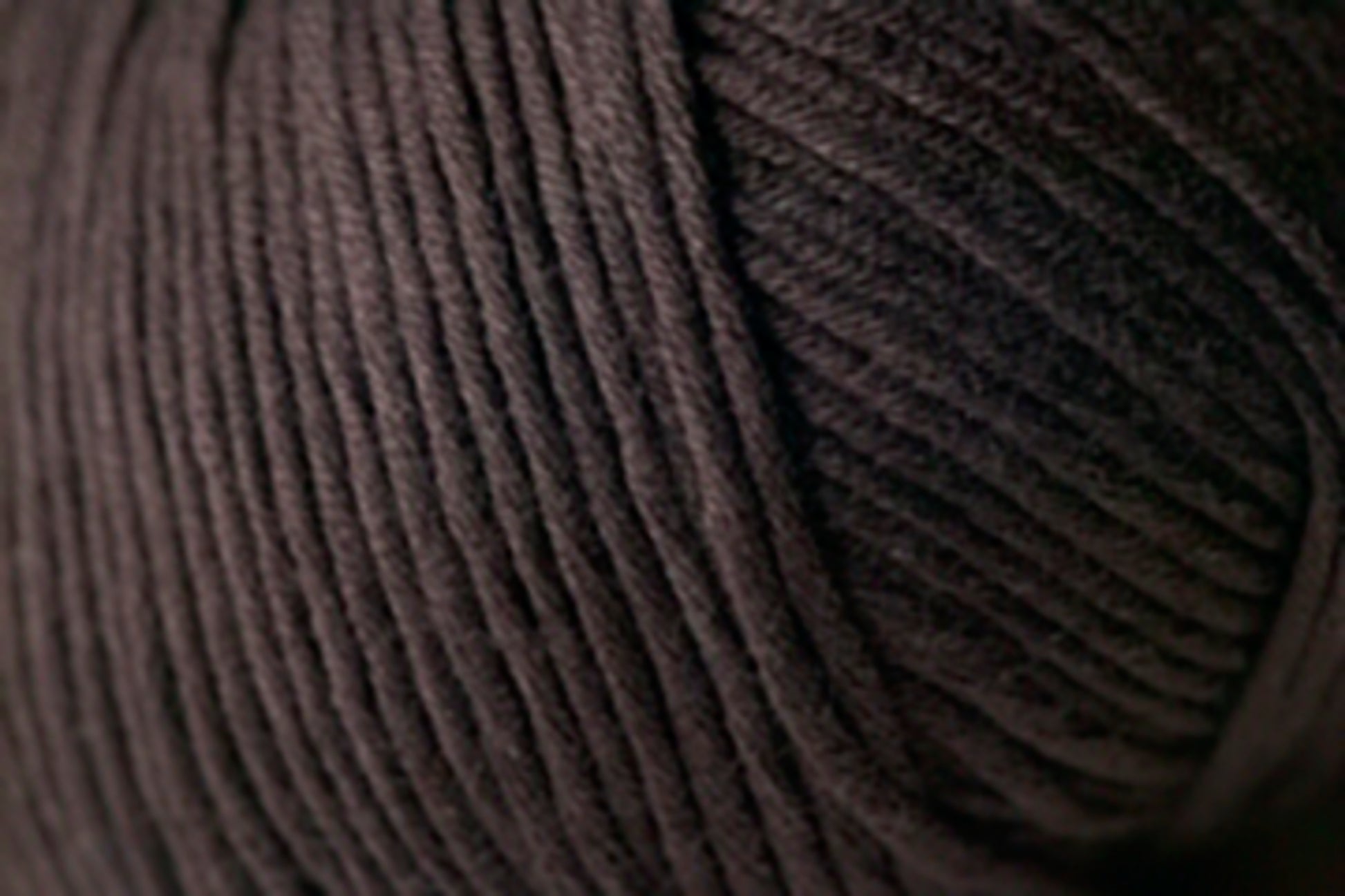 A close-up image of Jo Sharp Soho Summer DK Cotton from Kingfisher Yarn & Fibre. The strands are tightly wound, forming a dense, textured surface with visible lines and ridges in a deep shade of brown or black. Despite its rich hue, the lightweight cotton adds an unexpected touch of summer yarn versatility.