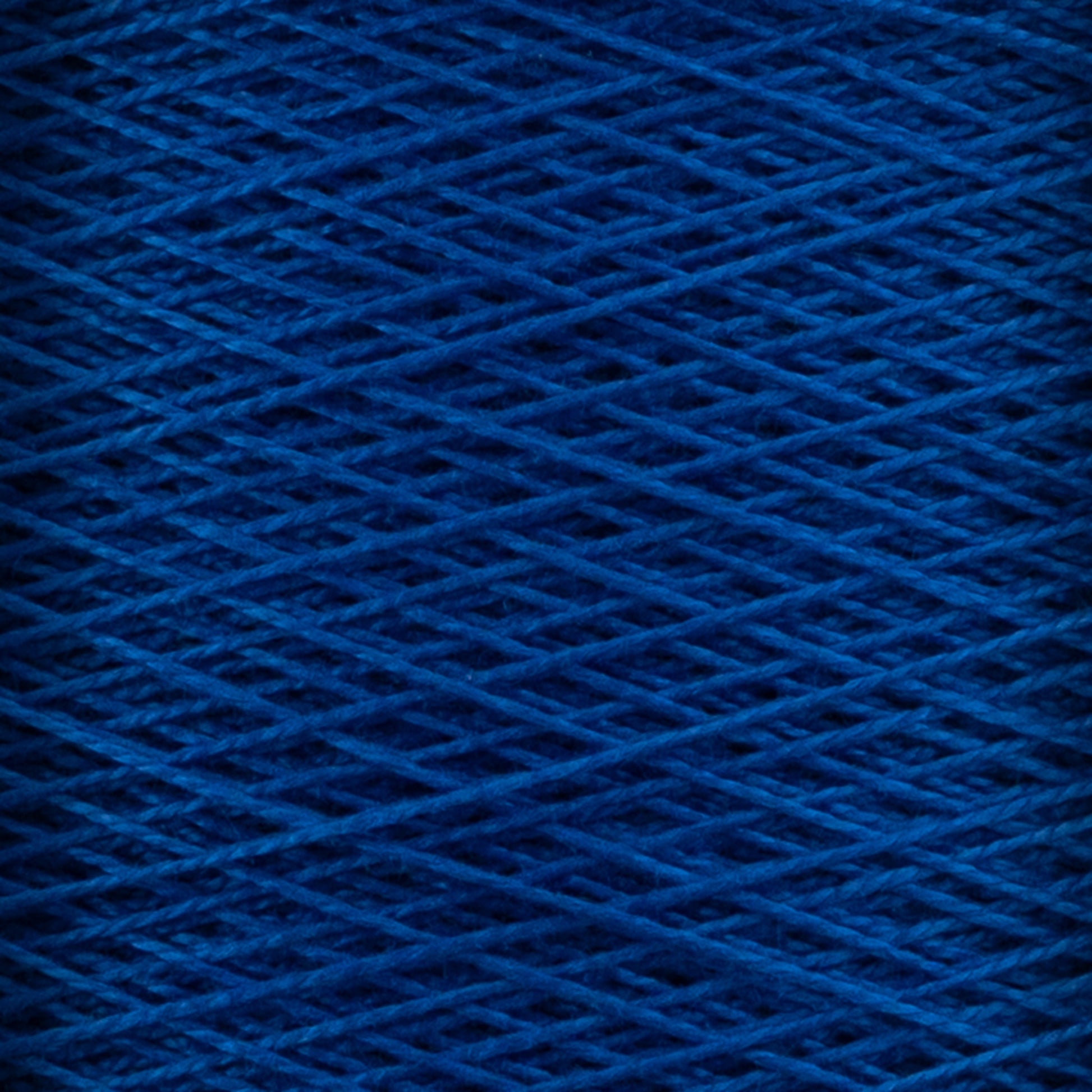 Close-up image of Supreme Corp's 10/2 Pearl Cotton Yarn in dark blue, wound in a crisscross pattern. The texture of this versatile mini-cone yarn is clearly visible, showcasing its fibrous and intertwined nature. The deep blue color is rich, uniformly distributed throughout the strands, and exhibits excellent colorfastness.