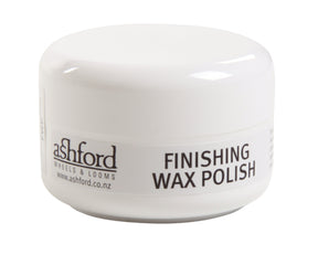 A small white container of Ashford Wax Polish - (75 ml) sits elegantly, showcasing the Ashford Handicrafts Limited logo and product name "WAX POLISH." Known for its environmentally-friendly formula, this rejuvenating product comes with a secure screw-on lid and features a website URL (www.ashford.co.nz).