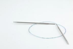 A pair of Skacel's Addi Turbo Circular Knitting Needles, showcasing silver metal short circular needles linked by a flexible blue plastic cable, lies crossed on a white background.