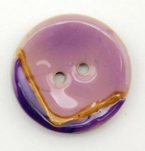 The Coco Boomerang 1 1/8" Button from Buttons Etc. is a round, purple ceramic button with a glossy shellac finish. It has two stitching holes and features a distinctive design: a brown stripe cutting across and a darker purple edge, set against a plain white background.