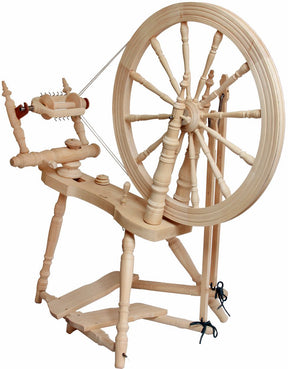 A wooden Saxony style spinning wheel, the Kromski Symphony Spinning Wheel by Kromski North America showcases a large wheel on one end and a detailed working area with various parts and mechanisms on the other side. This exquisite piece is designed for spinning fiber into yarn, boasting a traditional, handcrafted appearance.