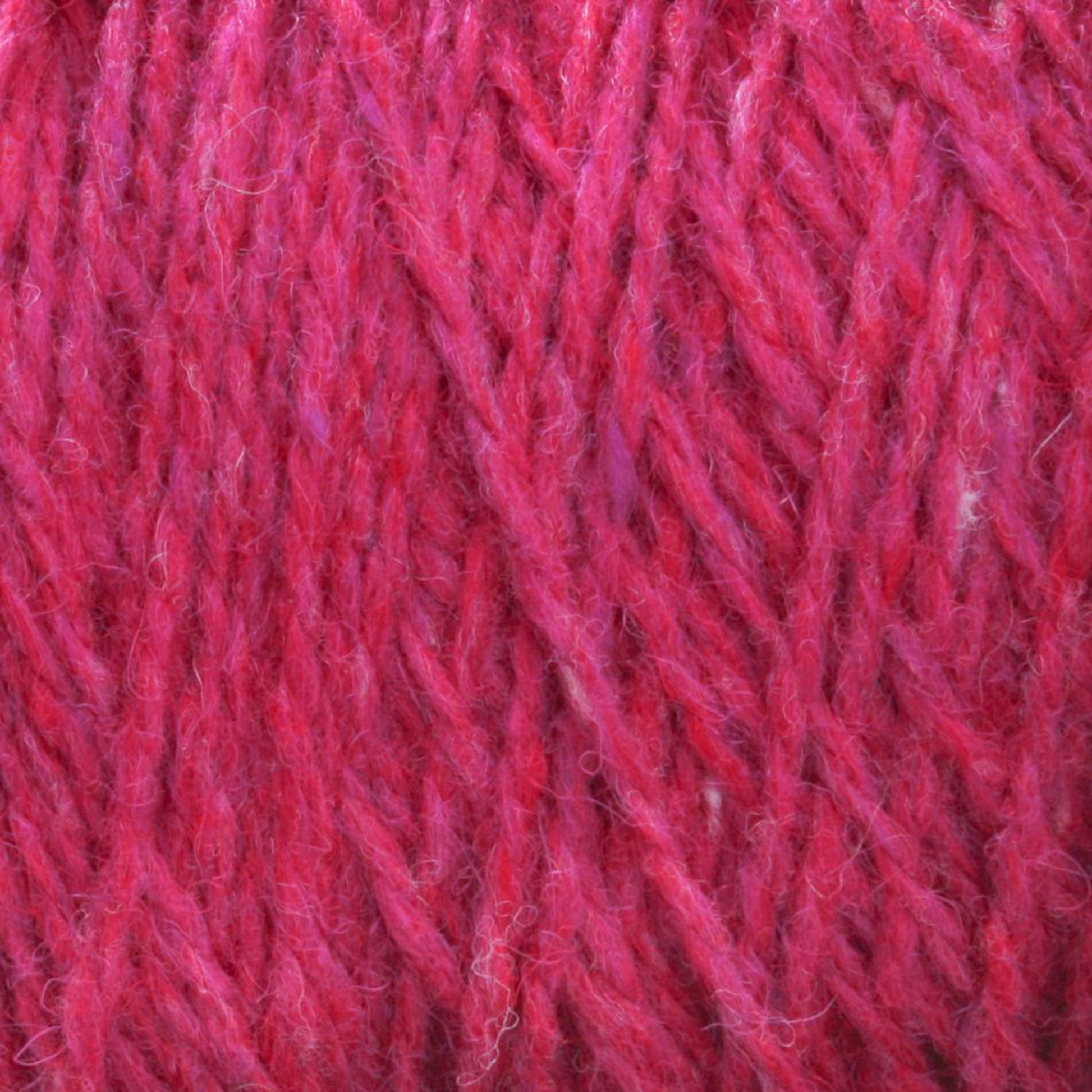 Close-up of Harrisville Designs' Shetland Yarn - Unwashed Cones. The yarn appears fluffy and soft, with a mix of darker and lighter red tones creating a textured and rich visual effect. The intertwining strands suggest a wool-blend material ideal for knitting lightweight blankets or Fair Isle knitting designs.