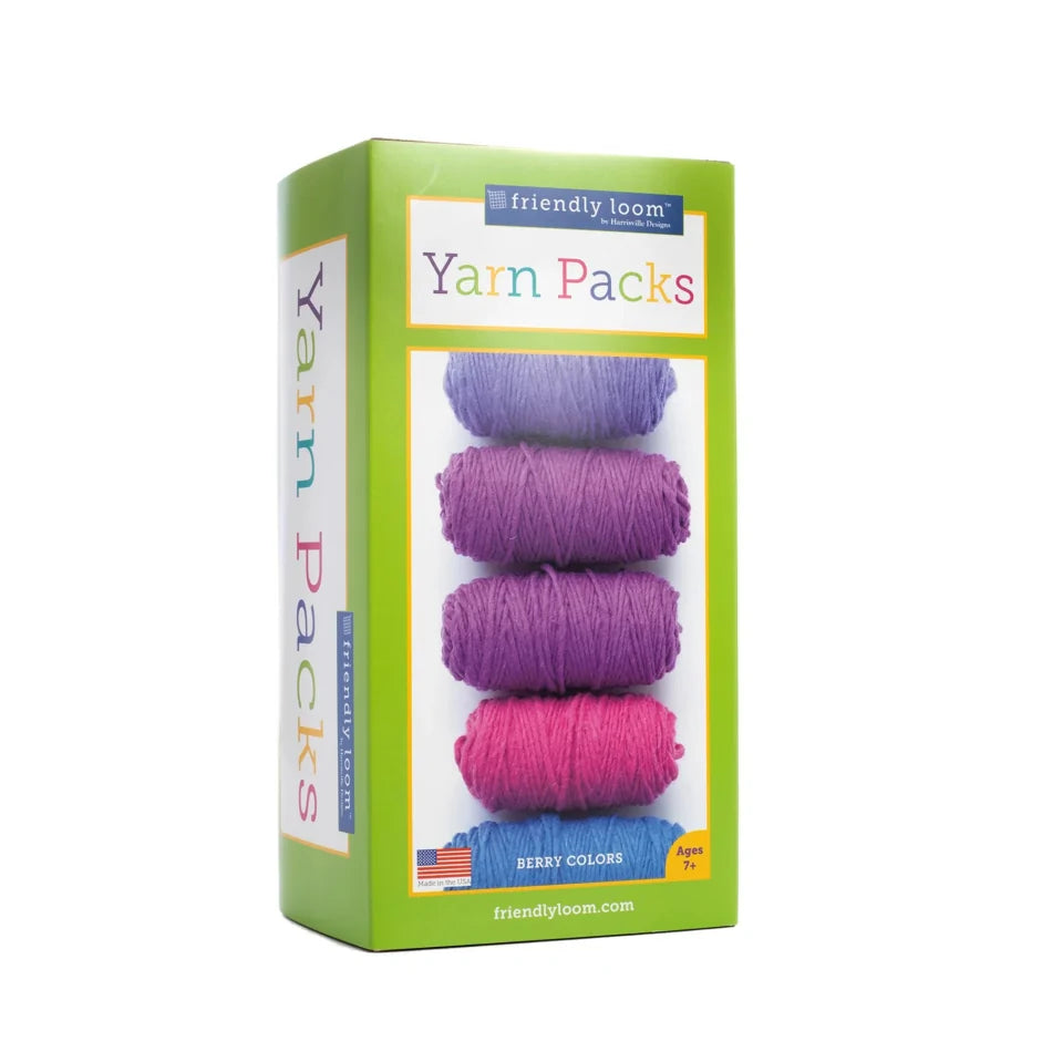 A box of "Lap Loom Yarn Pack, 6 Balls" from "Friendly Loom" is shown in the "Berry Colors" variant. The front of the box features six skeins of designer yarn in different shades of purple and pink, stacked vertically. Made from 100% wool, the pack is suitable for ages 7 and up and perfect for use with a peg loom. Proudly made in the USA.