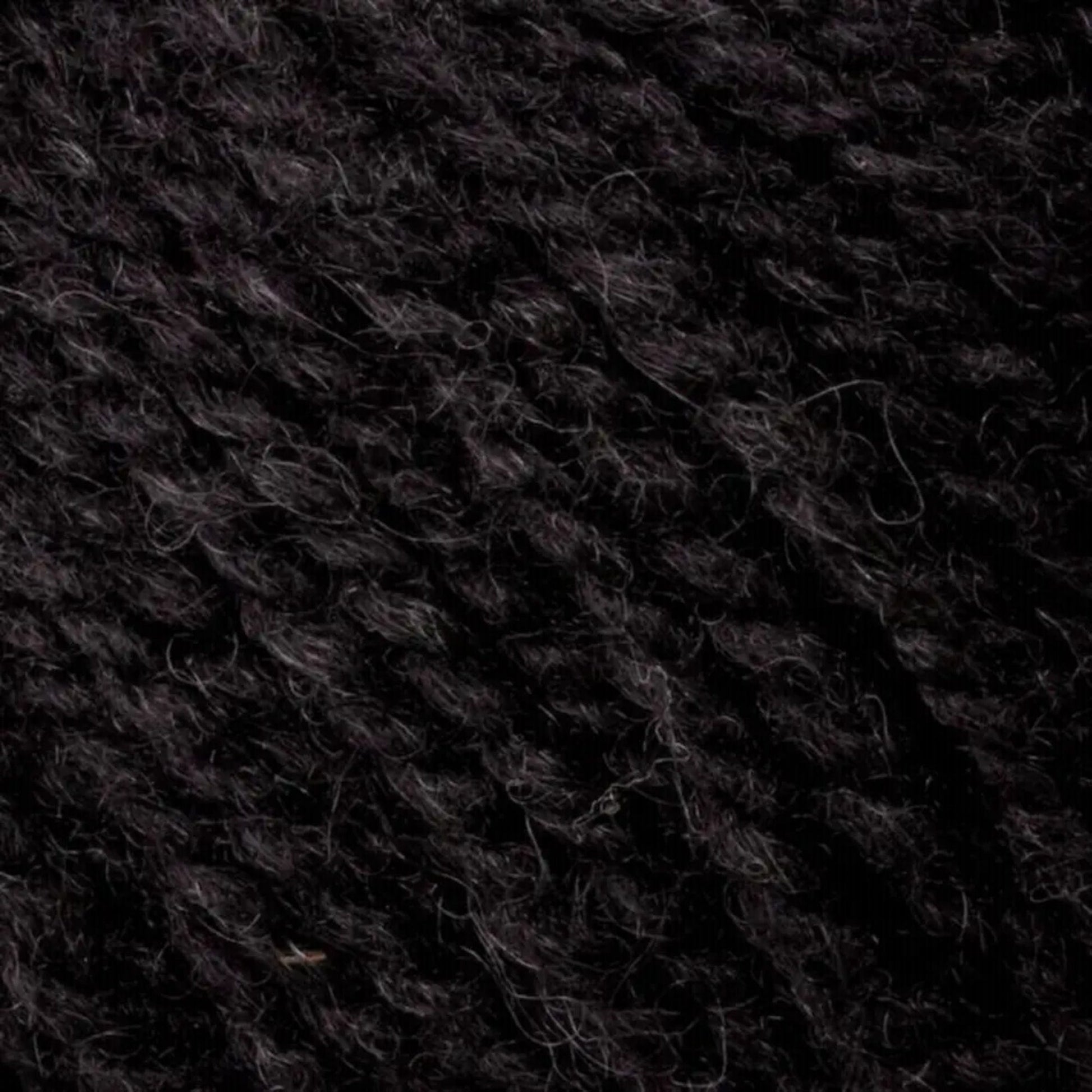 A close-up of Bartlettyarns' Bartlett Maine Wool in Sport Weight Cones reveals tightly woven, dark black fibers with a homespun look, subtle texture, and shading variations.