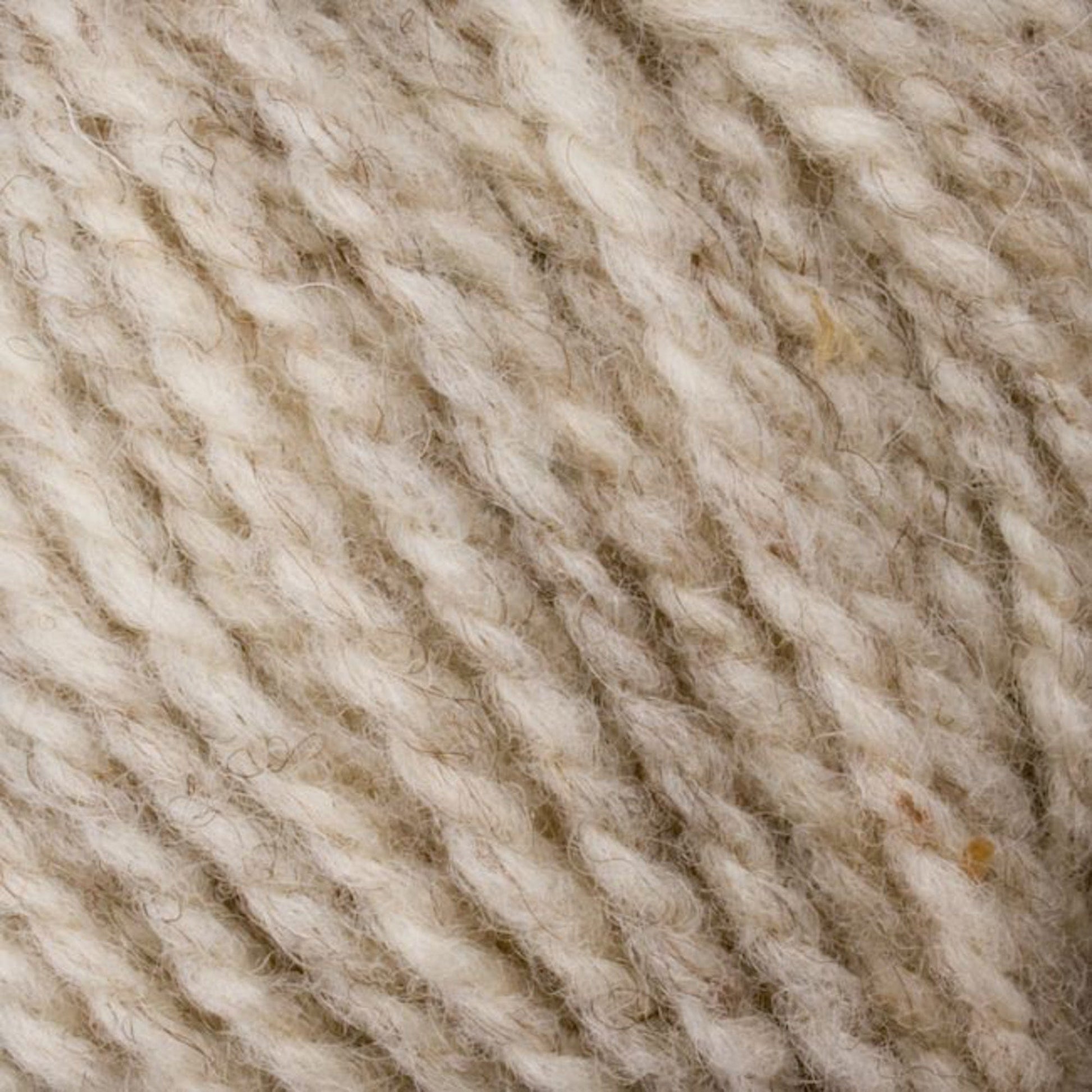 A detailed view of cream-colored Bartlett Maine Wool, Sport Weight Cones by Bartlettyarns, reveals textured yarn strands intertwined with light and slightly darker fibers. The wool appears soft and fluffy with a natural, homespun look that exudes rustic charm.