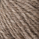 A close-up of Bartlettyarns' Bartlett Maine Wool, Sport Weight Cones showcases its homespun appearance with soft, textured fibers in light brown and beige. The fluffy, thick yarn is ideal for knitting or crocheting cozy garments.