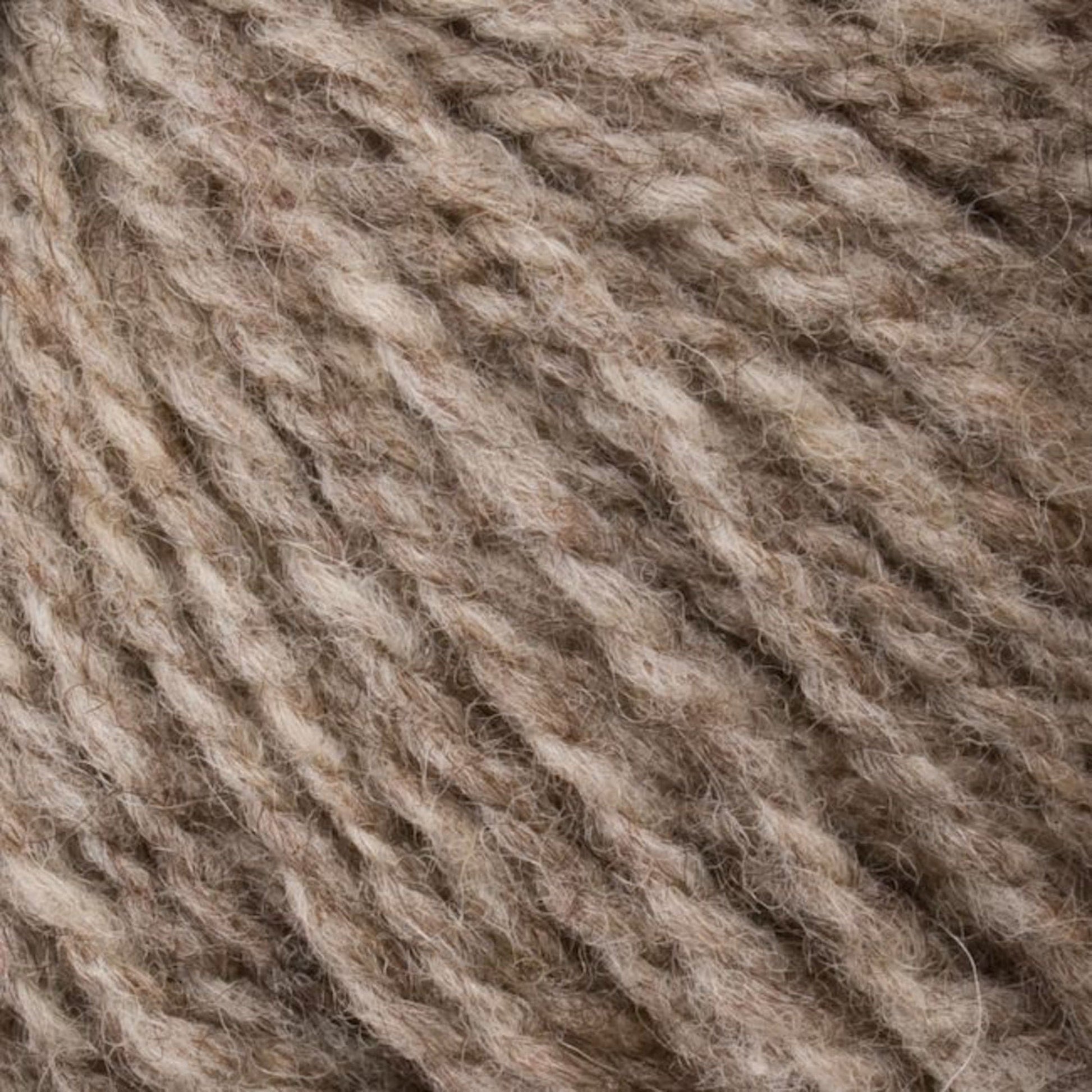 A close-up of Bartlettyarns' Bartlett Maine Wool, Sport Weight Cones showcases its homespun appearance with soft, textured fibers in light brown and beige. The fluffy, thick yarn is ideal for knitting or crocheting cozy garments.