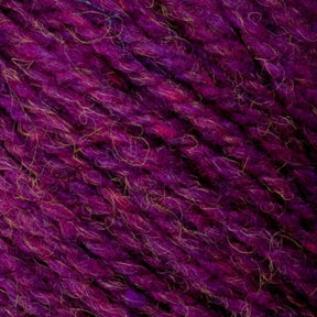 Close-up of Bartlettyarns' Bartlett Maine Wool, Sport Weight Cones in textured purple shades with homespun appearance, magenta hints, and a slightly fuzzy look from small fibers. This thick, soft yarn is ideal for knitting or crocheting projects.